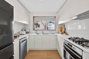 Eine moderne Küche mit weißen Schränken, einem Edelstahlkühlschrank, einem Gasherd und einem Fenster mit Außenblick.