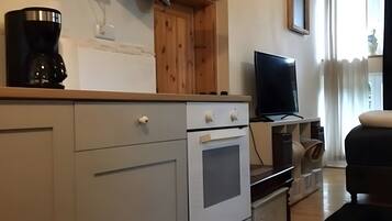 A kitchen with a coffee maker, a TV on a stand, and a wooden cabinet.