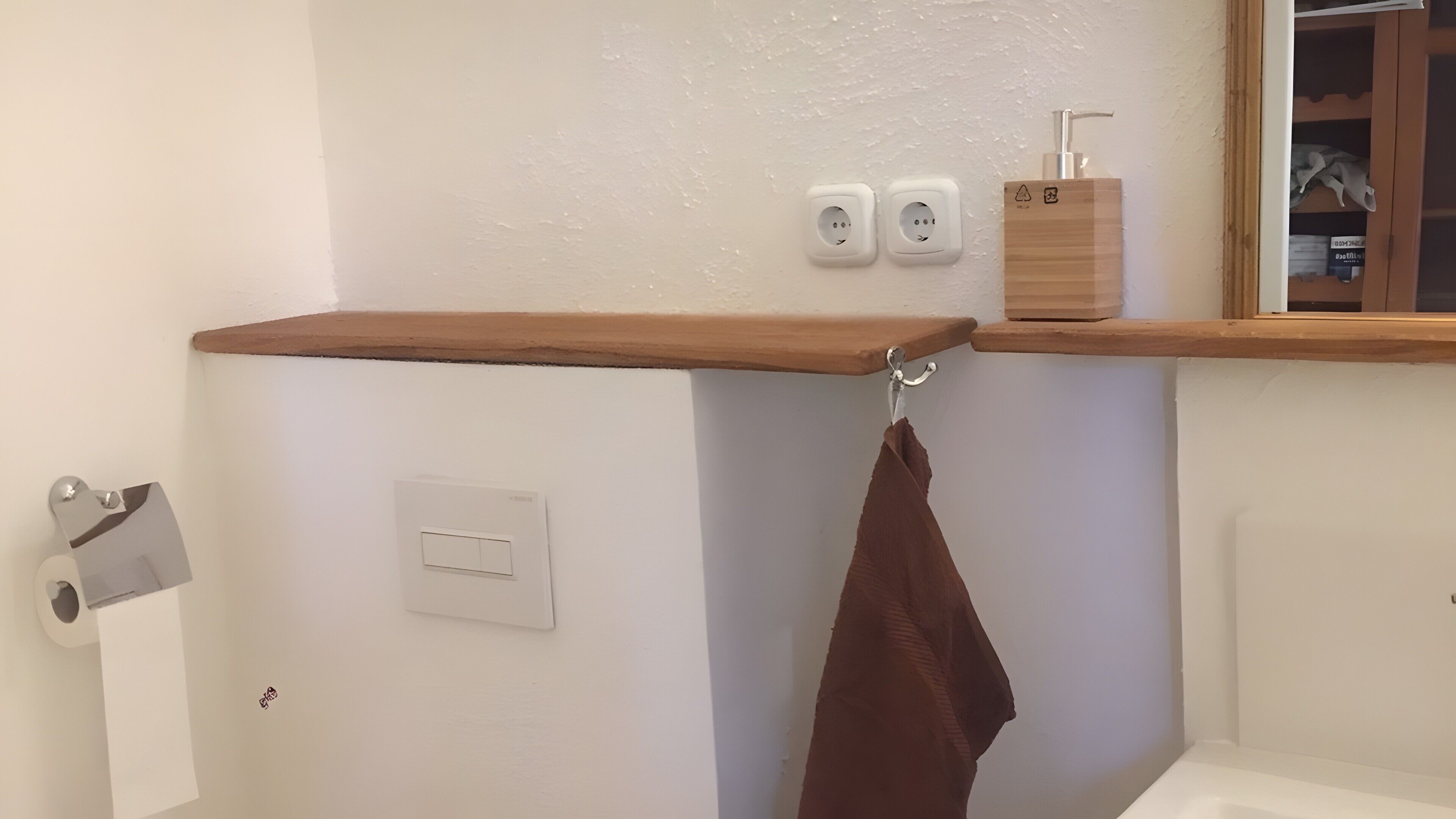 A bathroom with a wooden shelf, two electrical outlets, a towel rack, and a toilet paper holder.