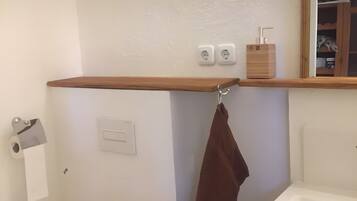 A bathroom with a wooden shelf, two electrical outlets, a towel rack, and a toilet paper holder.