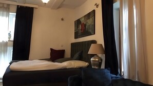 Una camera d'albergo con un letto, una lampada, un quadro e una finestra con tende.