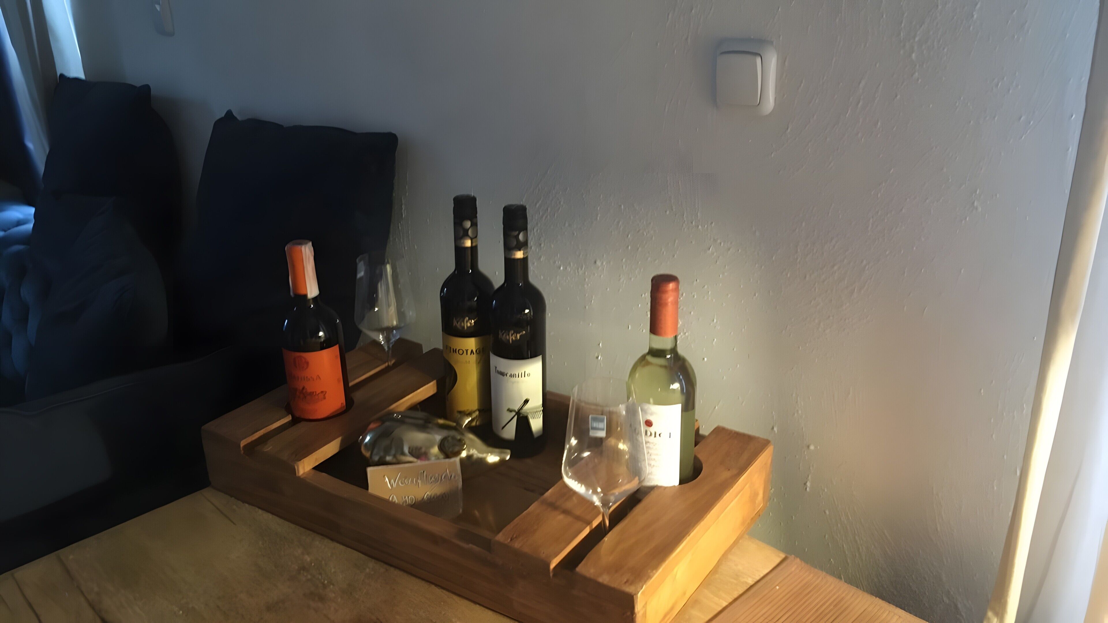 A wooden tray with wine bottles and glasses on a table.