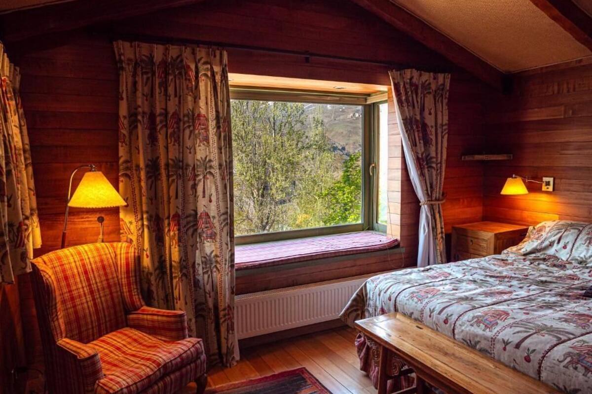 Ein gemütliches Zimmer mit einem Bett, einem Sessel, einem Fenster mit Vorhängen und zwei Lampen.