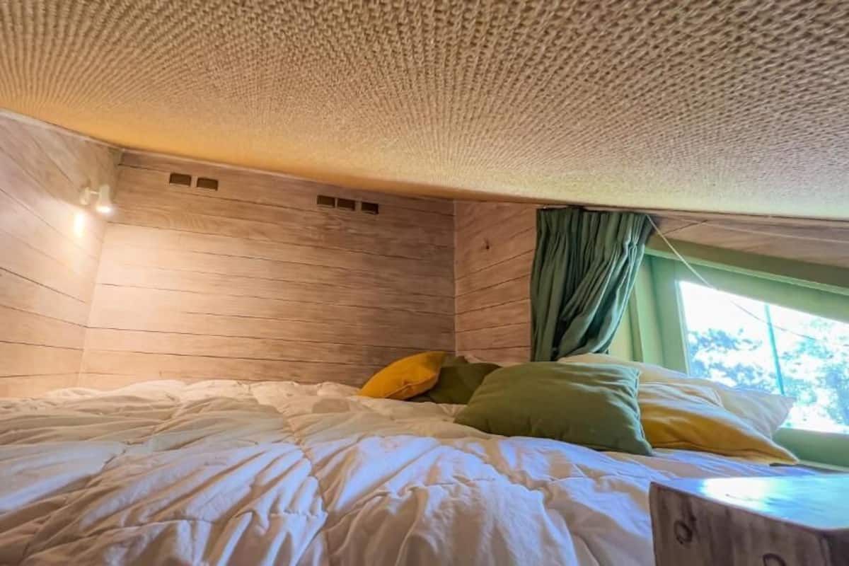 Ein Zimmer mit Holzboden, einem Bett mit weißer Bettwäsche und einem Fenster mit grünen Vorhängen.