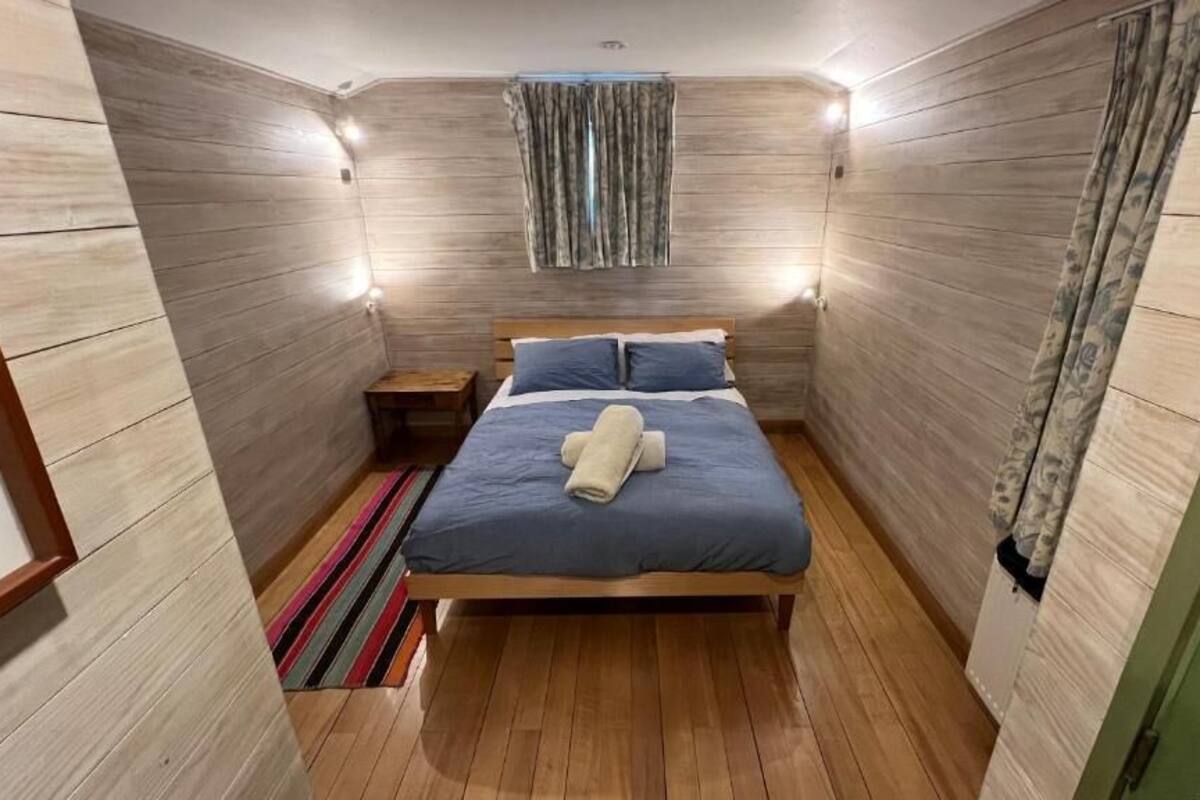 Ein Schlafzimmer mit einem Holzbett, einem Nachttisch, einem Streifen Teppich und einem Fenster mit Vorhängen.