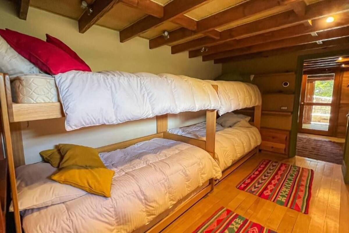 Ein Schlafraum mit Etagenbetten, Holzbalken, Holzboden und einem gemusterten Teppich.