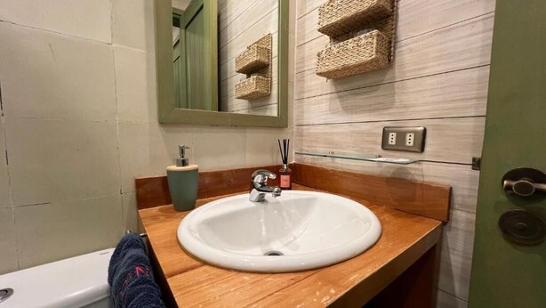 Une salle de bain avec un lavabo blanc, un miroir, un meuble-lavabo en bois, une serviette et une porte verte.