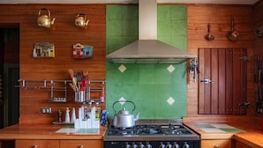 Μια κουζίνα με ξύλινα ντουλάπια, μια κουζίνα αερίου, έναν απορροφητήρα από ανοξείδωτο ατσάλι και πράσινα πλακάκια στον τοίχο πάνω από τον πάγκο.