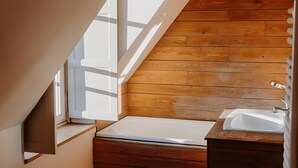Een kleine badkamer met schuine balken, een houten vloer, een raam en een wastafel.