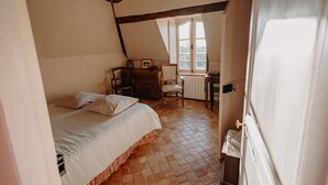 Een slaapkamer met een bed, een stoel, een dressoir en een raam.