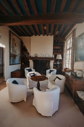 Un salon chaleureux avec des fauteuils blancs, une cheminée, des étagères à livres et un grand tableau.