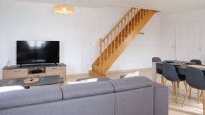 A modern living room with a flat-screen TV, a wooden staircase, a dining area, and a grey sofa. - La Maison Angèle. (Criel-sur-Mer)
