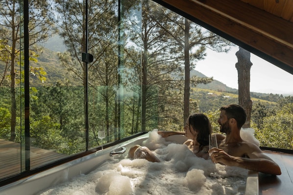 A couple in a hot tub with a scenic forest view.