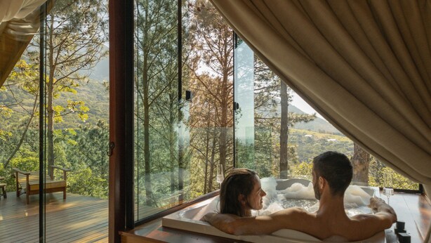 A couple in a hot tub with a scenic view of trees and hills.