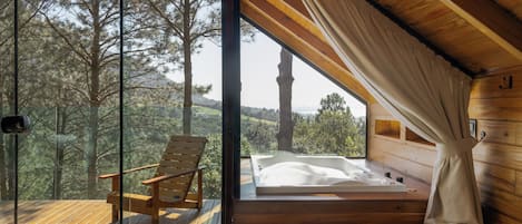 A wooden cabin with a glass door leading to a balcony, a wooden chair, and a hot tub.