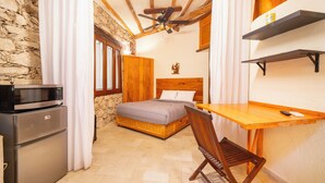 Habitación compacta con cama, un escritorio de madera, una silla, microondas y refrigerador.
