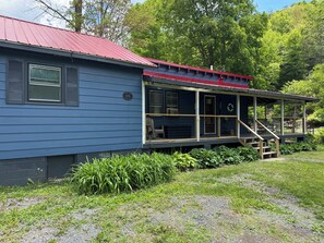 A blue house with a red roof, a porch with a railing, and a number plate.