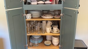 A kitchen cabinet with shelves containing kitchenware, including plates, bowls, and glassware.