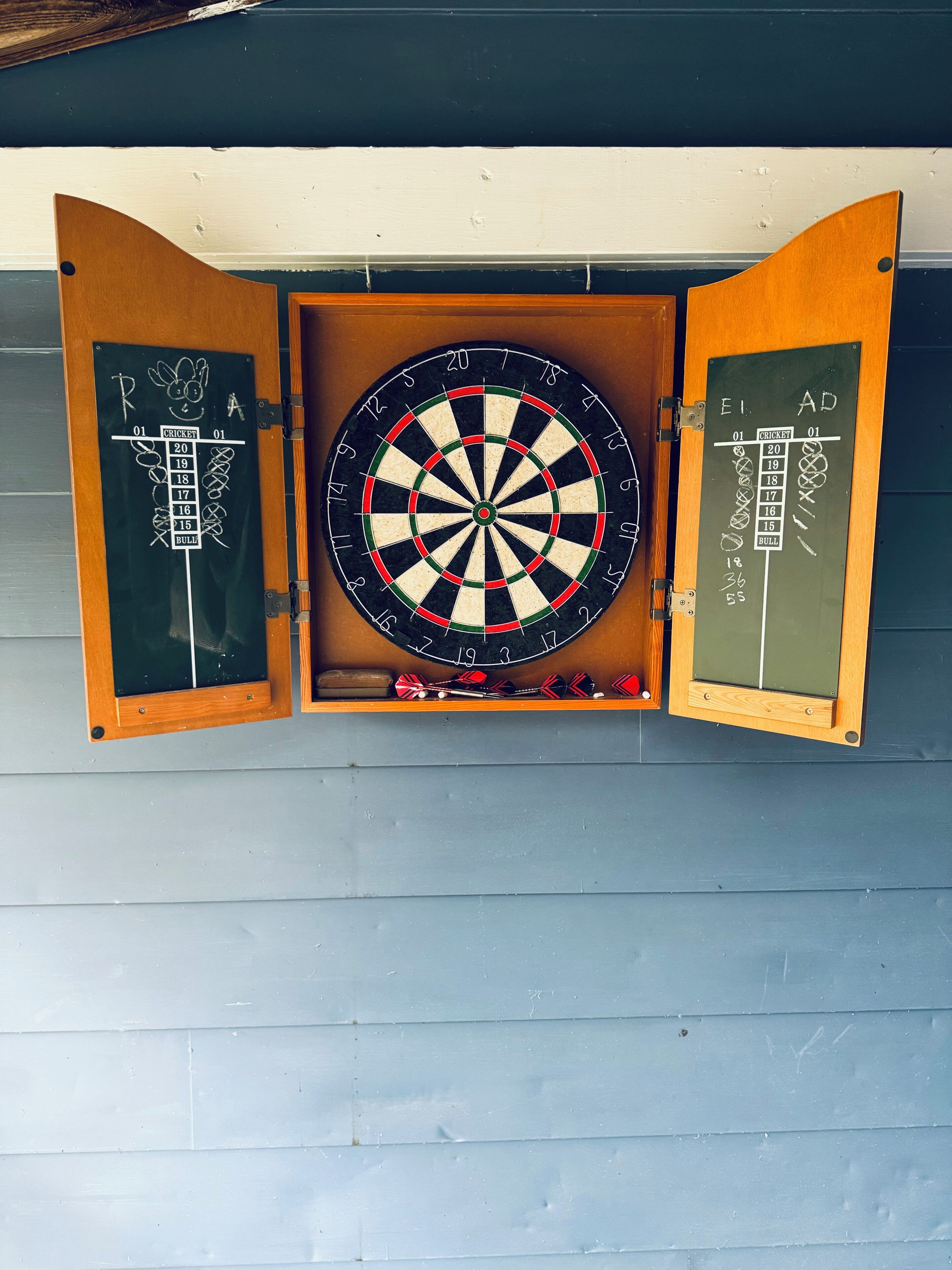 A dartboard mounted on a wall with two chalkboards on either side.