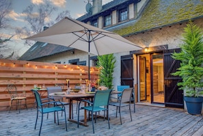 Une terrasse extérieure avec une table et des chaises, un grand parasol et une clôture en bois.