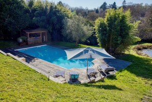 Une piscine rectangulaire dotée d’une terrasse en bois, entourée de pelouse et d’arbres.