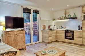 Une cuisine moderne avec des meubles de rangement en bois, un four encastré et un téléviseur posé sur un meuble en bois.