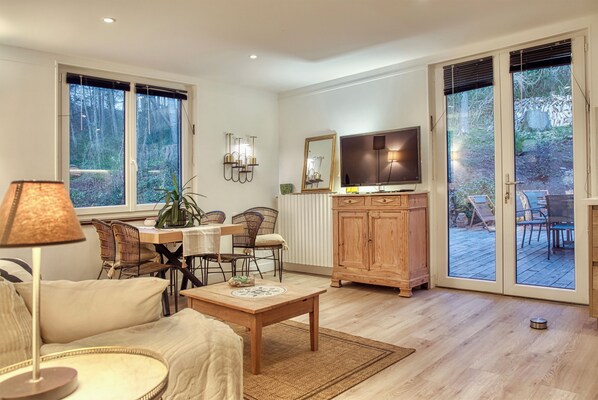 Un salon comprenant un canapé, une table basse, un téléviseur, une table à manger avec des chaises et un buffet en bois.