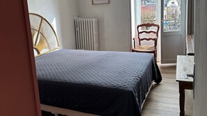 Ein Schlafzimmer mit Bett, Stuhl, Heizkörper, einem Bild an der Wand und Blick durch die Tür.