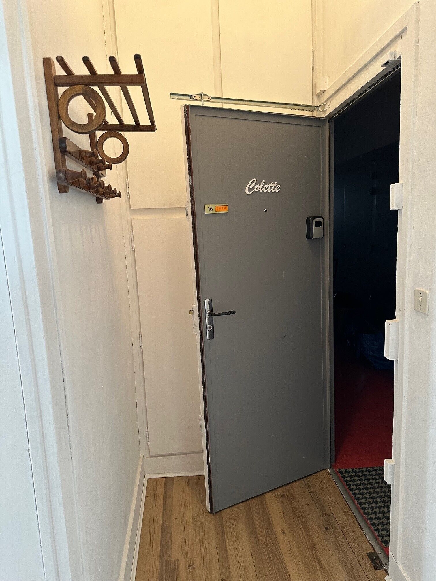 Una puerta gris con una placa que dice 'Colette', un perchero de madera y un picaporte.