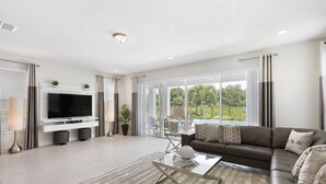 A modern living room with a flat-screen TV, a glass coffee table, a brown sofa, and a large sliding glass door leading to an outdoor area. - Last Minute Disney Getaway! Private Pool, Hot Tub & Game Room. Book Now! #15070 (Orlando)
