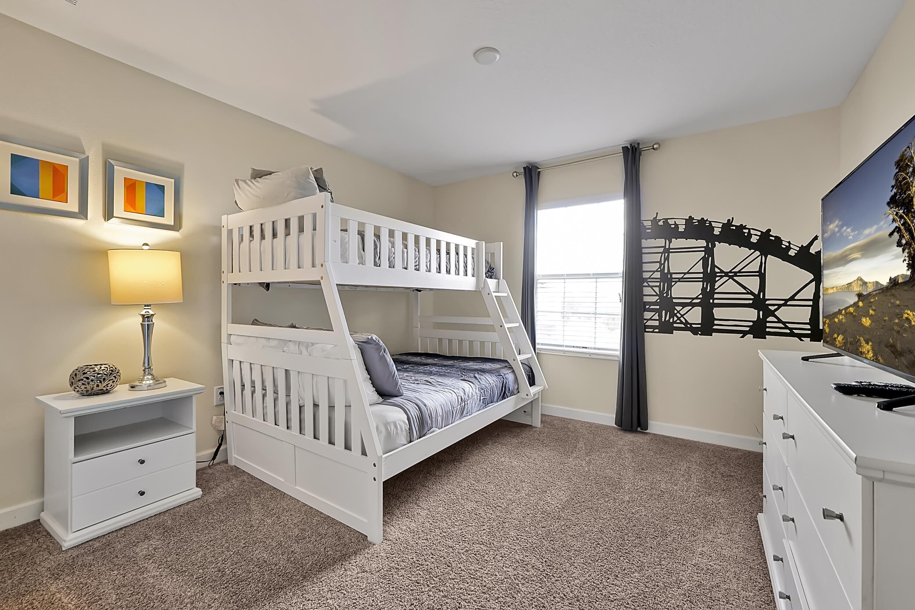 A bunk bed room with a nightstand, lamp, and dresser.