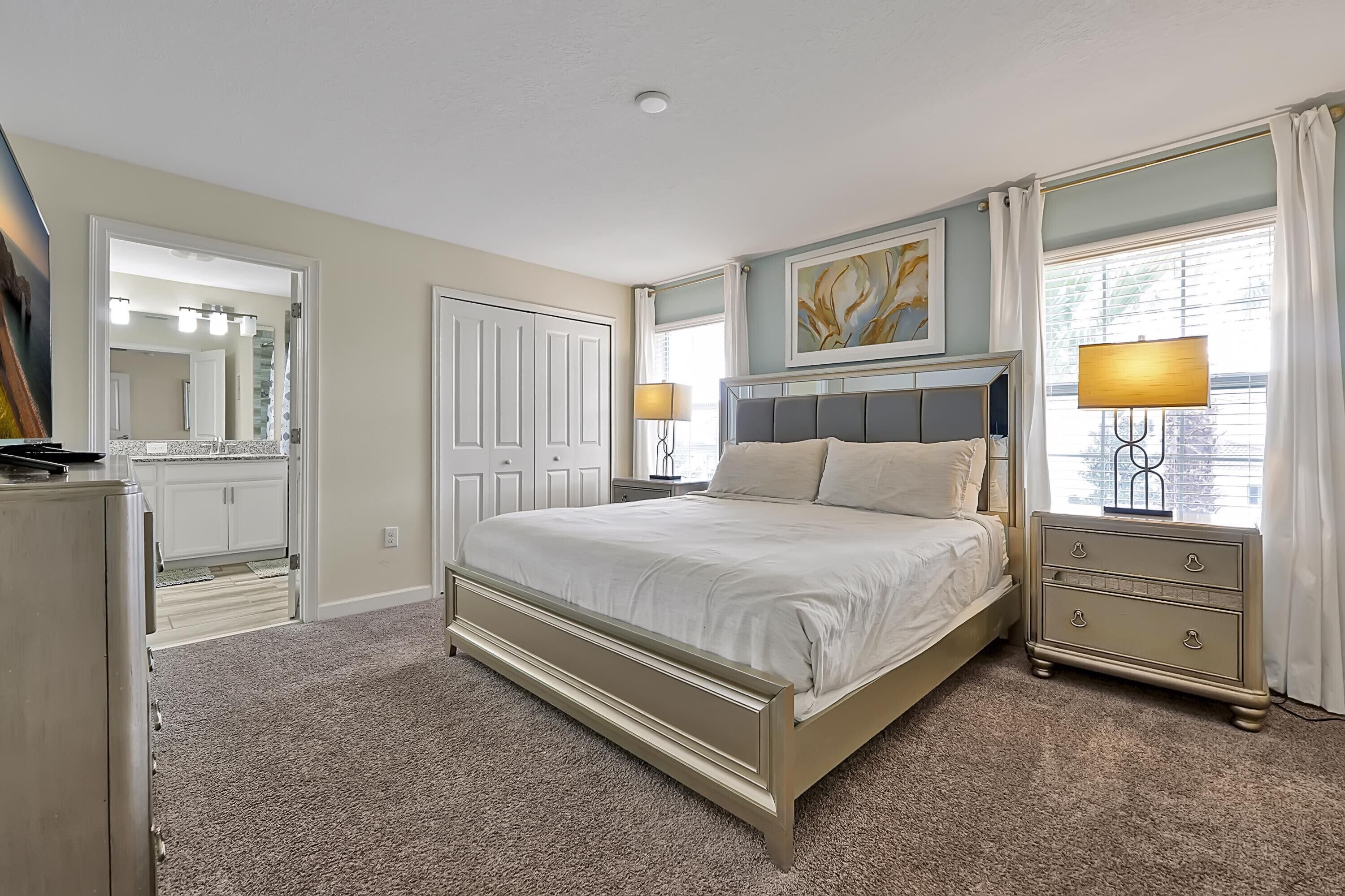 A bedroom with a bed, dresser, nightstand, lamp, and a painting on the wall.