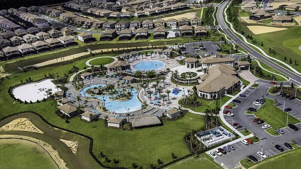 Vue aérienne d’un quartier résidentiel avec une piscine centrale, un parking et un réseau routier.