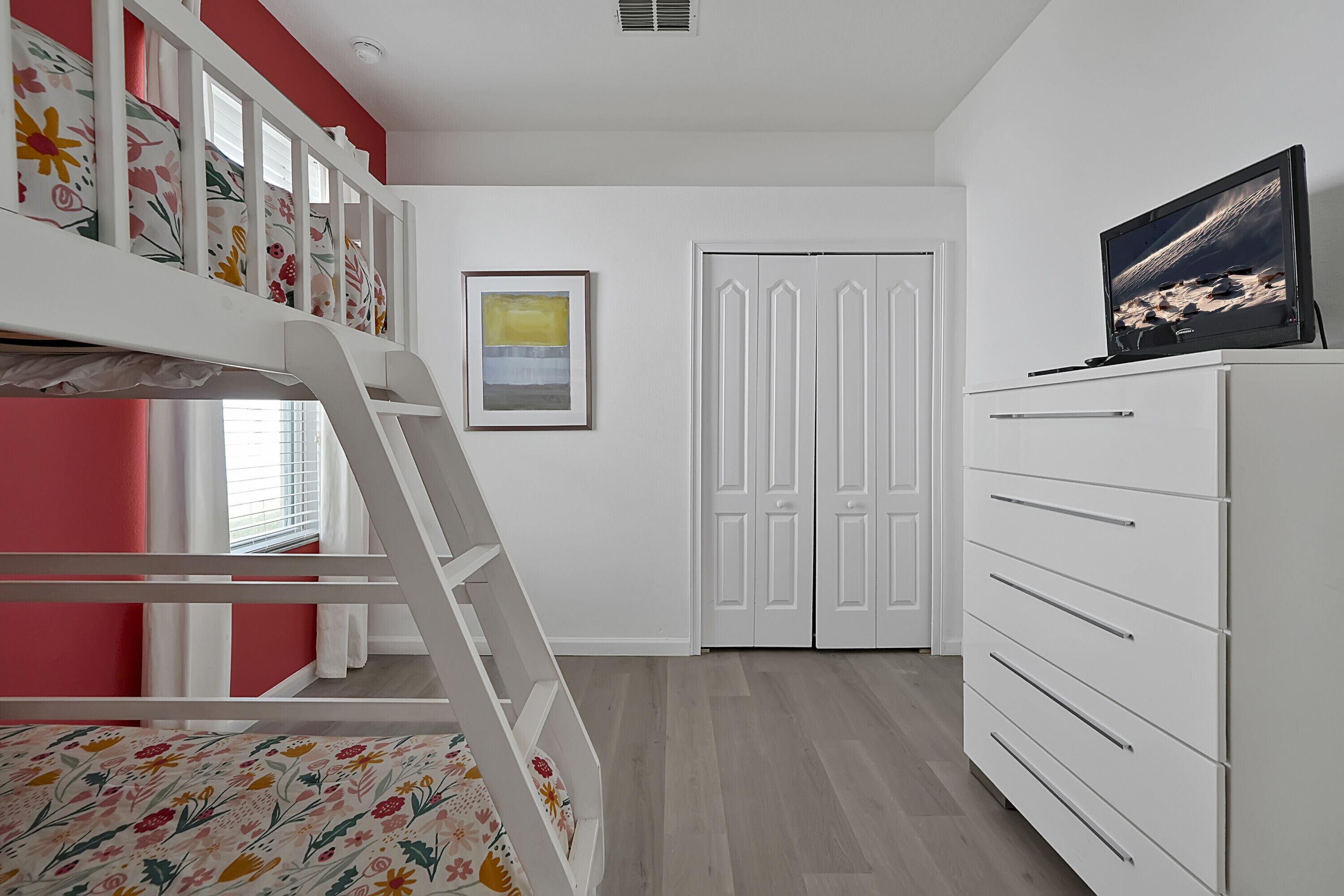Een slaapkamer met een stapelbed, een dressoir, een televisie en een deur.