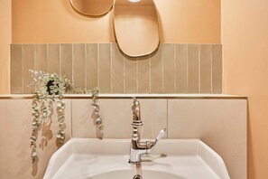 A bathroom with a white sink, a gold faucet, and a mirror above it. - Charming Duplex Center of Paris (Paris)