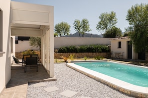 Uma área de piscina com terraço, mobiliário e vista para árvores e montanhas.