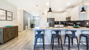 Uma cozinha moderna com uma ilha central, banquetas de bar e eletrodomésticos de aço inoxidável.