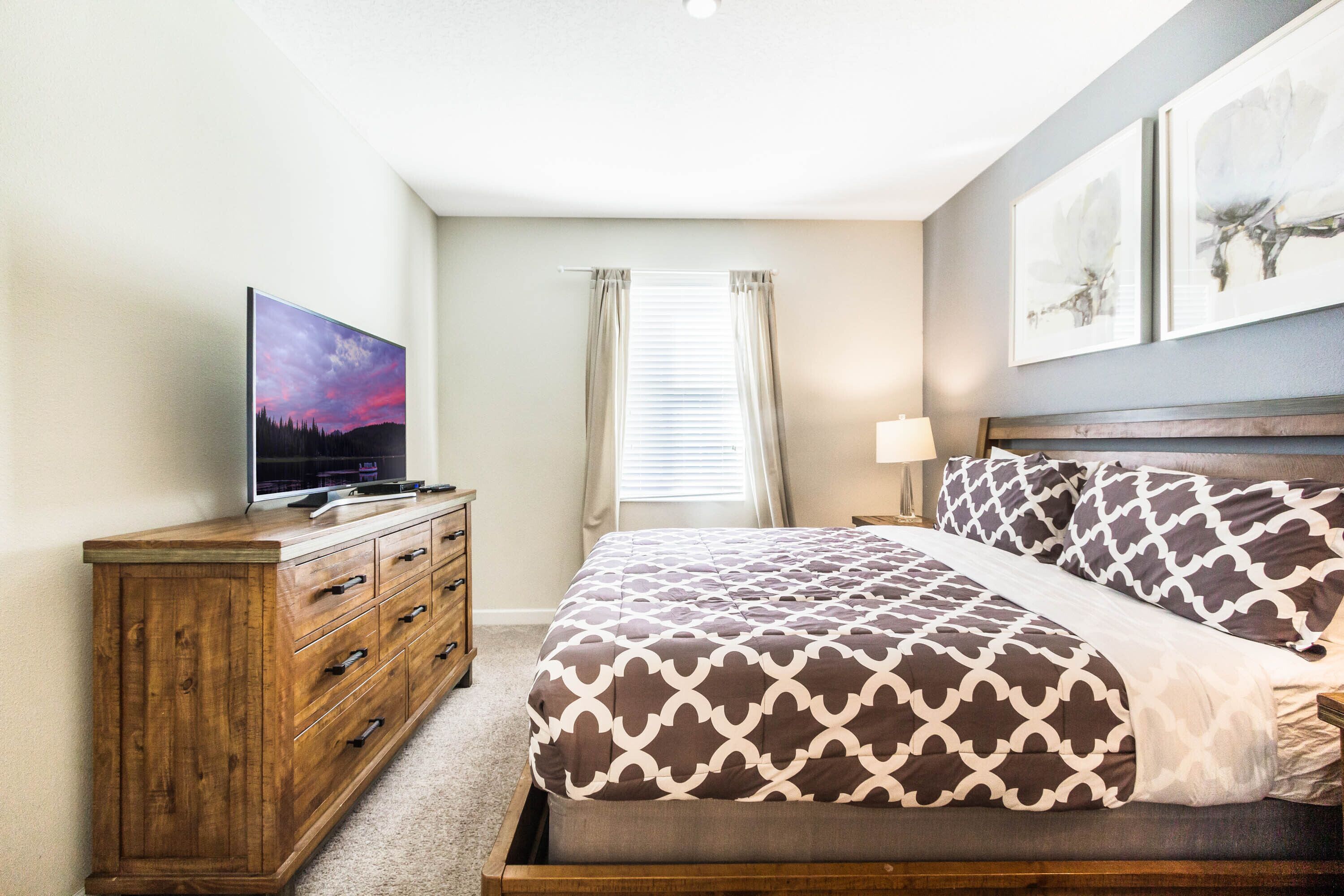 A bedroom with a bed, a wooden dresser, a television, and a window with curtains.