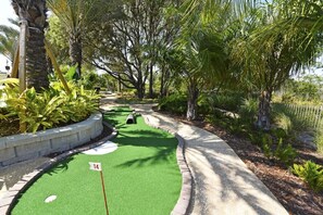 Ein Minigolfplatz mit einem grünen Spielbereich, einer Fahne, die Loch 14 markiert, und umliegenden Bäumen.