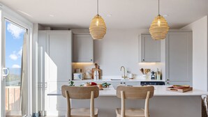 A modern kitchen with two wooden chairs, a central island, and pendant lighting. - The Lookout in Brixham (Brixham)