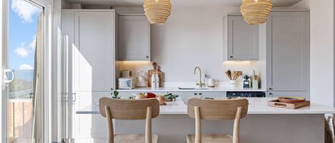 A modern kitchen with two wooden chairs, a central island, and pendant lighting.