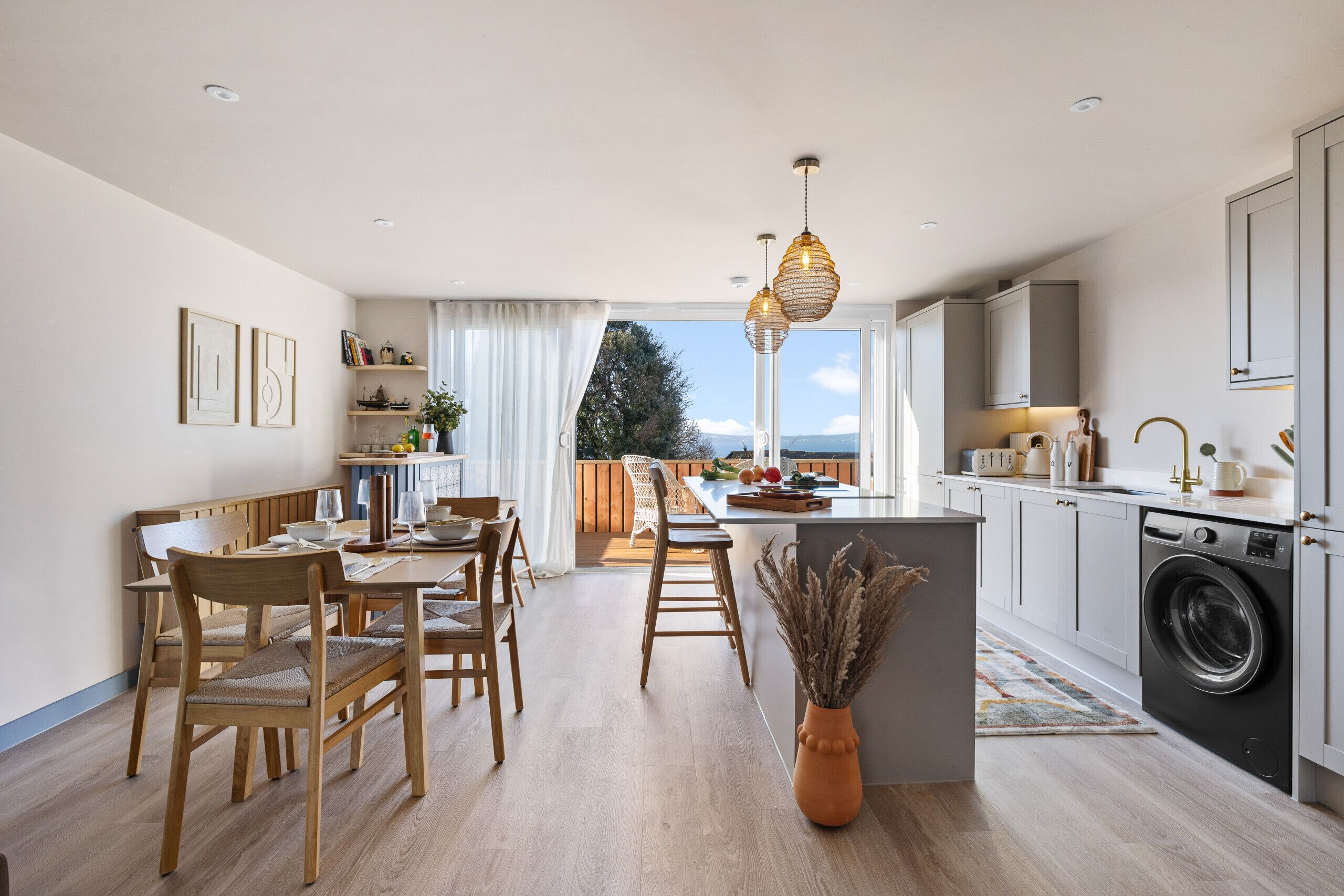 A modern kitchen with a dining area, large windows, and a view of the outdoors.