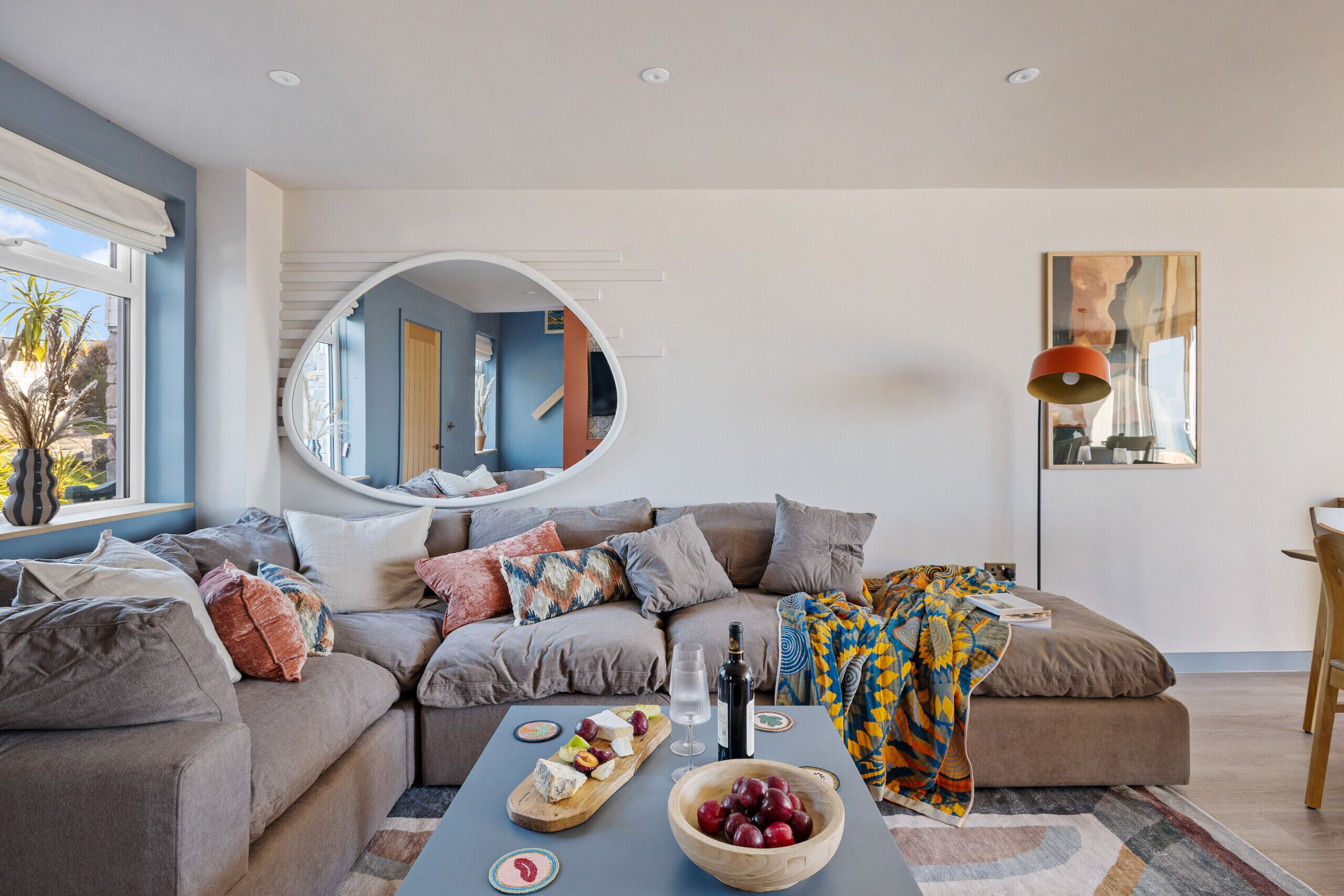 Ein modernes Wohnzimmer mit einer Couch, einem Couchtisch mit Snacks, einem Spiegel und einem Gemälde an der Wand.