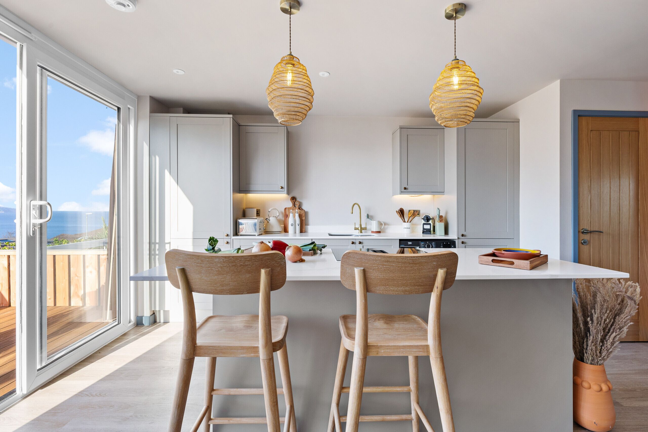A modern kitchen with two wooden bar stools, a large island, and pendant lighting.