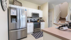 Una cocina moderna con electrodomésticos de acero inoxidable, armarios blancos, un microondas y un reloj en la pared.