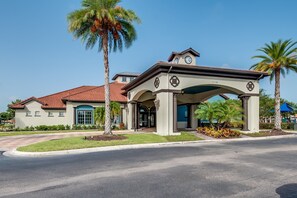 A two-story building with a red-tiled roof, a covered entrance with a clock, and palm trees. - Last Minute Disney Getaway! Townhouse with Private Pool. Book Now! #20202 (Orlando)