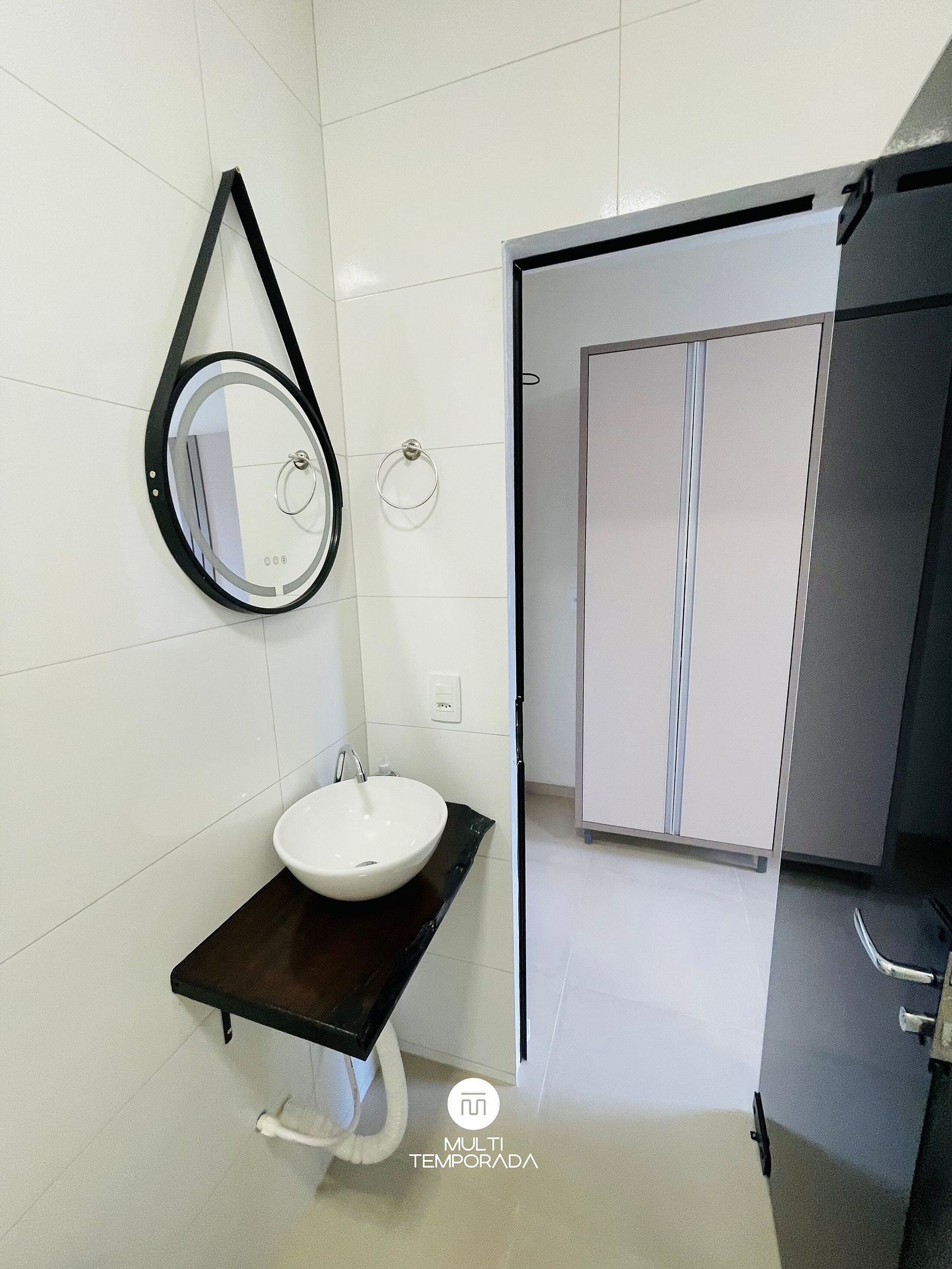 Une salle de bain moderne avec un lavabo blanc, un plan de toilette noir, un miroir rond et une cabine de douche en verre.