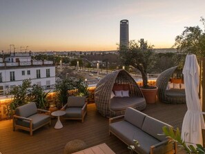 Eine Dachterrasse mit Sitzgelegenheiten und Blick auf die Stadt, im Hintergrund ein hohes Gebäude.