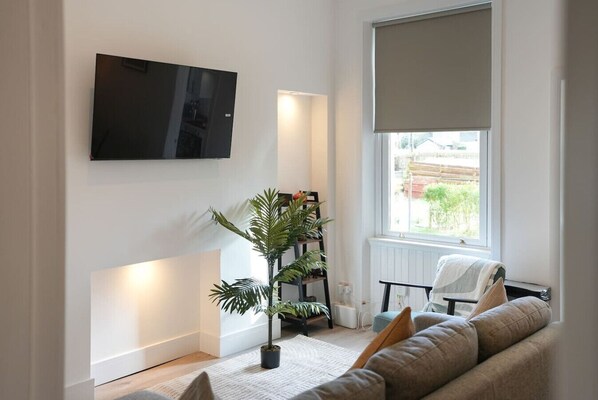 Sala de estar con televisor de pantalla plana, una planta en maceta, sofá y ventana con vistas.