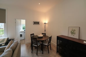 Un comedor con una mesa, sillas, una lámpara, un cuadro enmarcado y una lavandería visible a través de una puerta abierta.